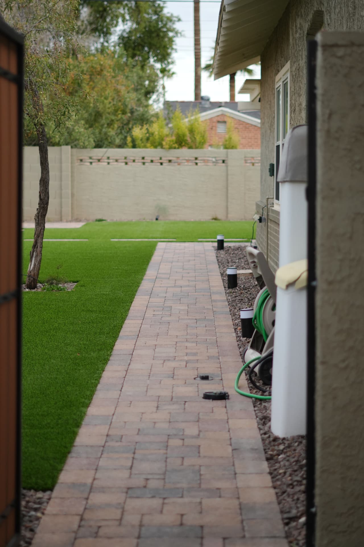 Paver walkway running between artificial turf and a gravel strip along the house