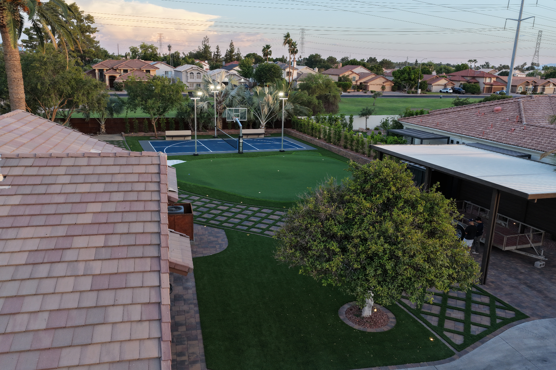 Putting green with bunker wrapping around a blue sport court at dusk