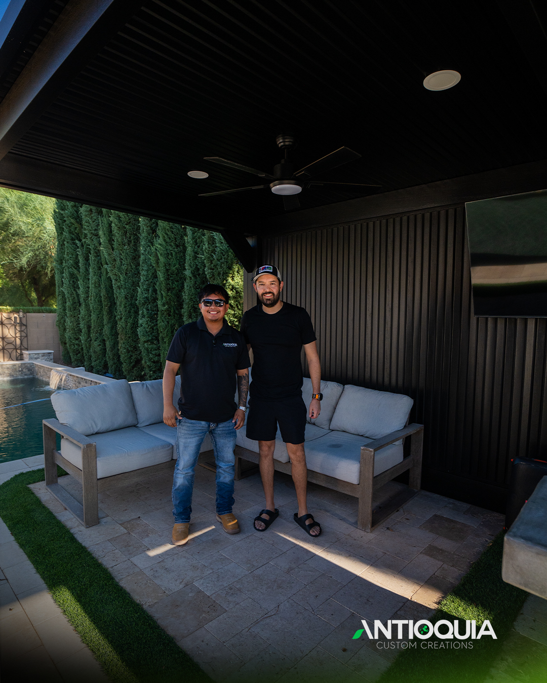 Two people standing under the finished covered patio with slatted wall and TV