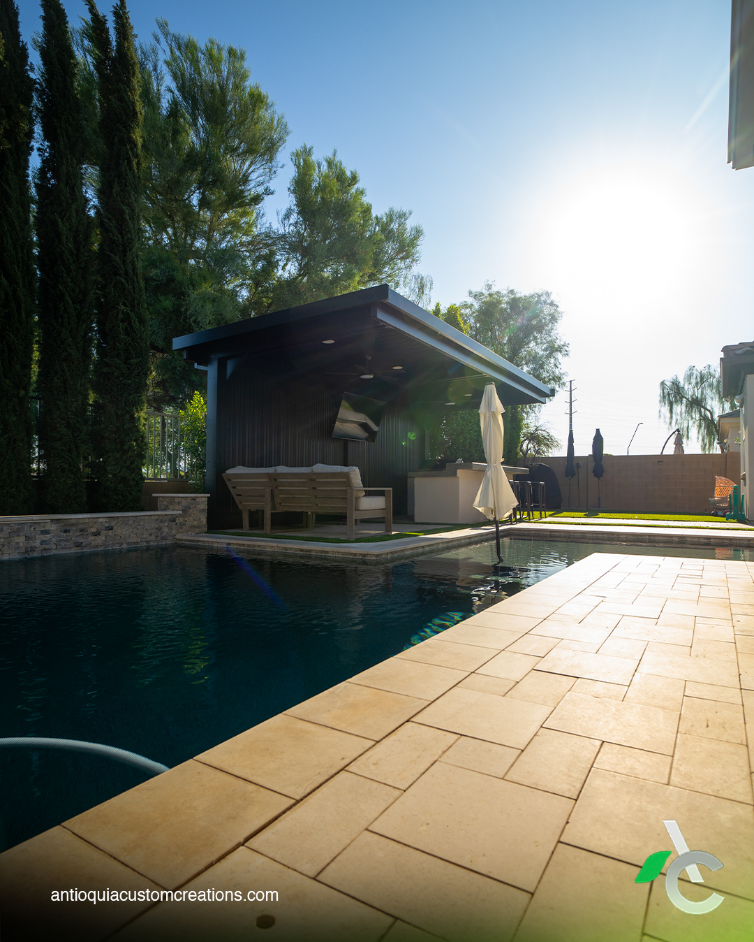 Pool with travertine decking looking toward a black cabana pavilion