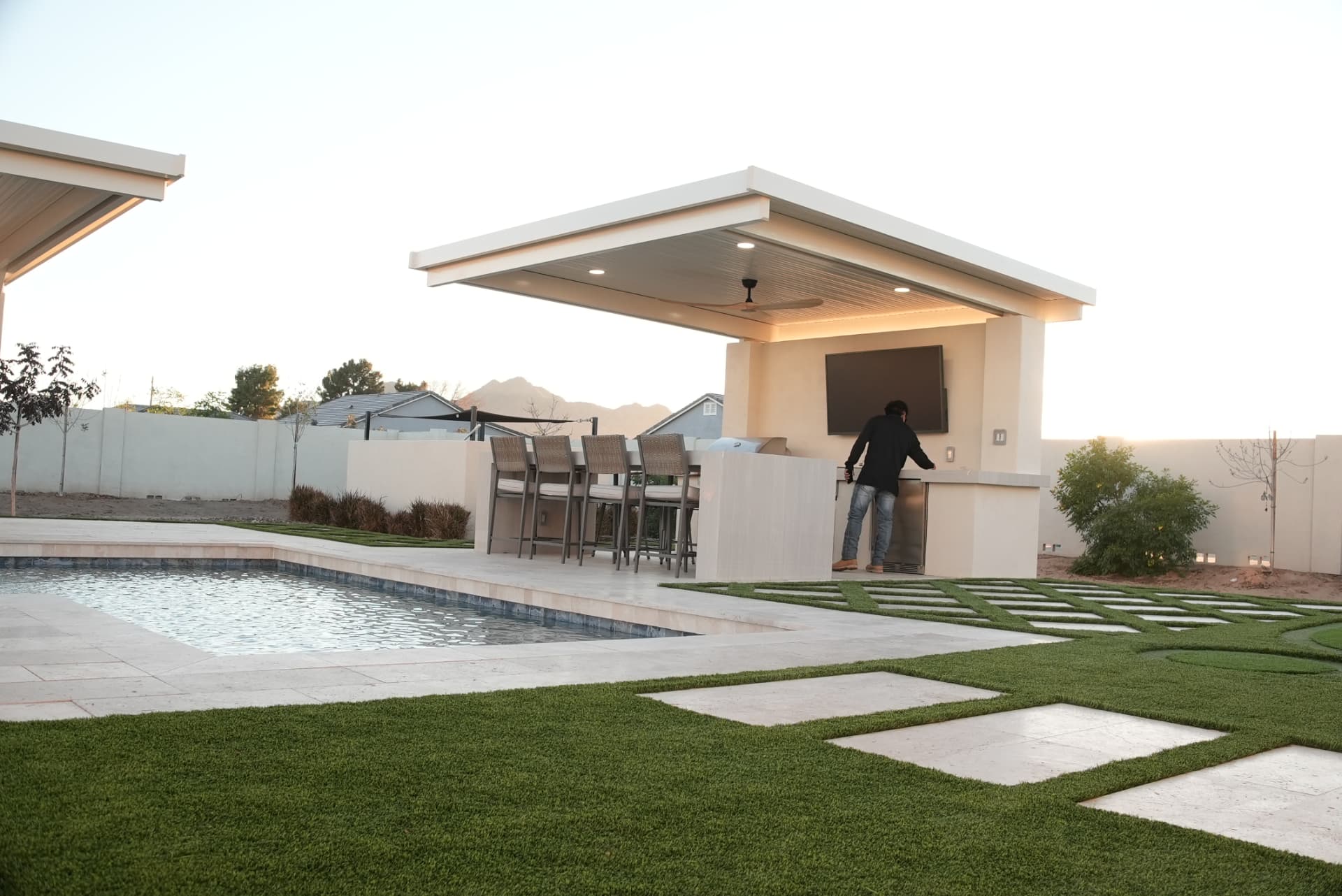 Person at an outdoor bar beside a pool with turf paver walkway