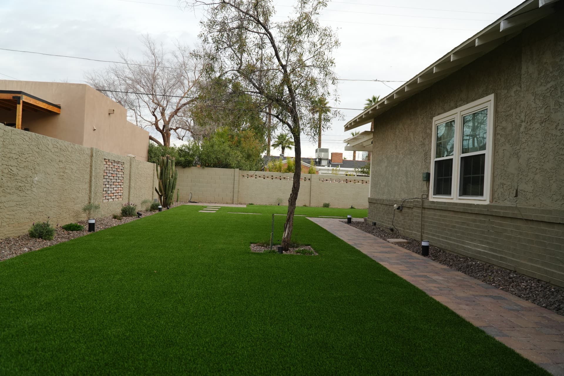 Backyard artificial turf lawn with paver perimeter path and planting beds