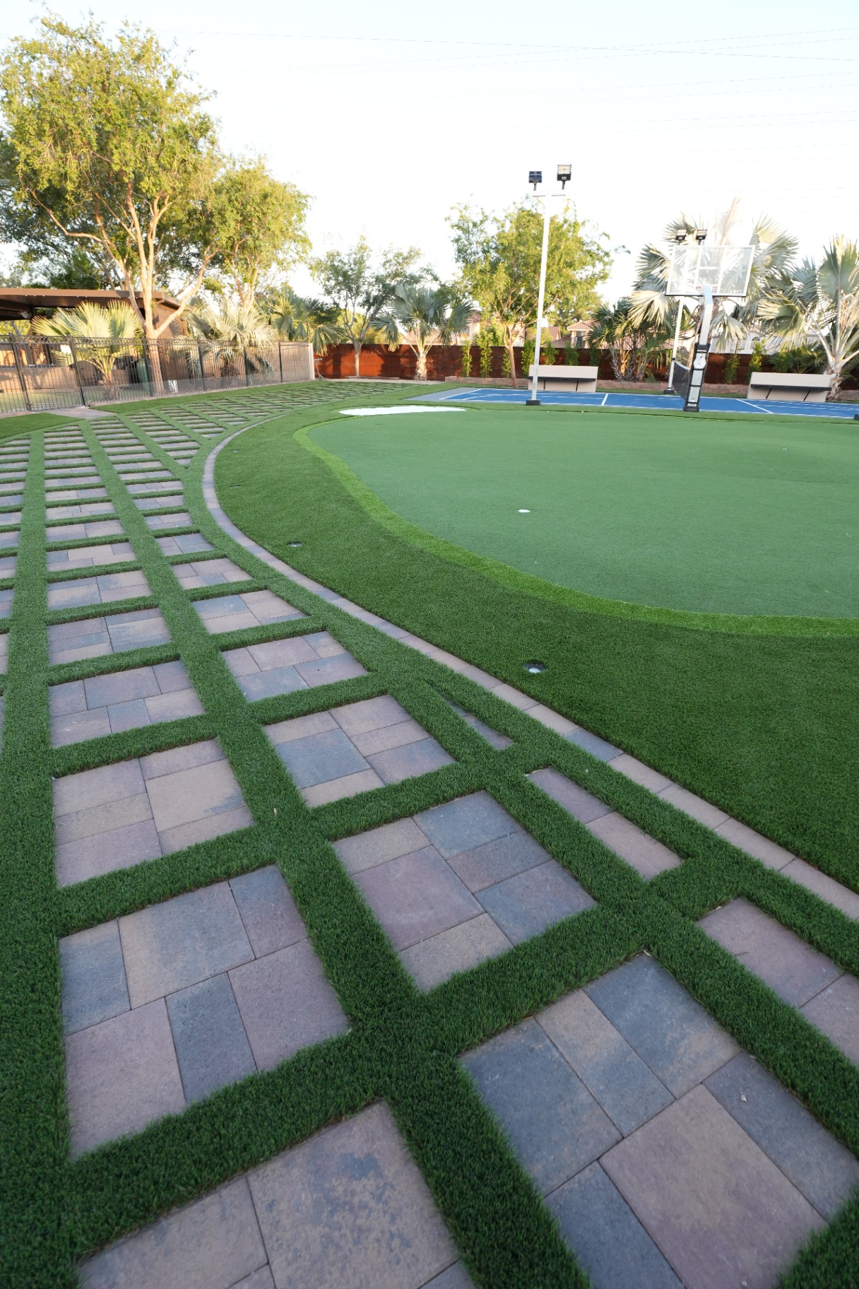 Turf-jointed paver grid curving into a putting green beside a sport court