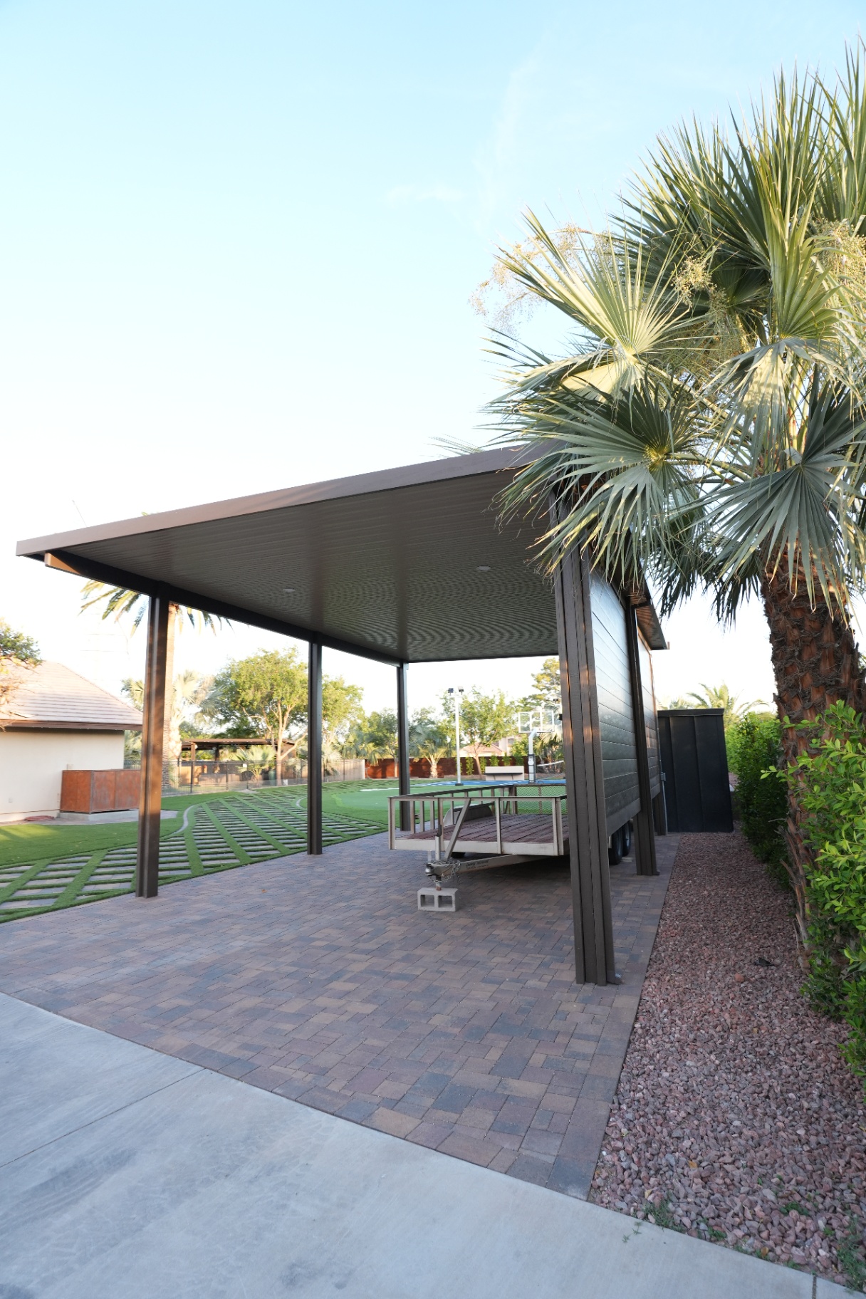 Modern flat roof shade structure over a paver pad with palm tree