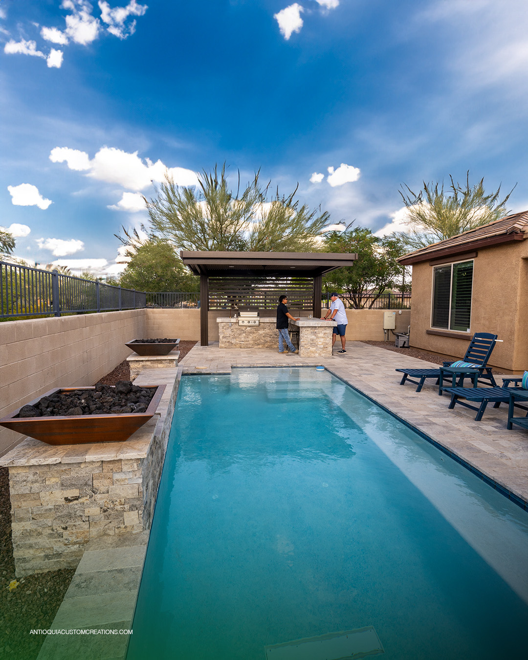Long view of a rectangular pool with fire bowls and a pavilion in a Peoria backyard
