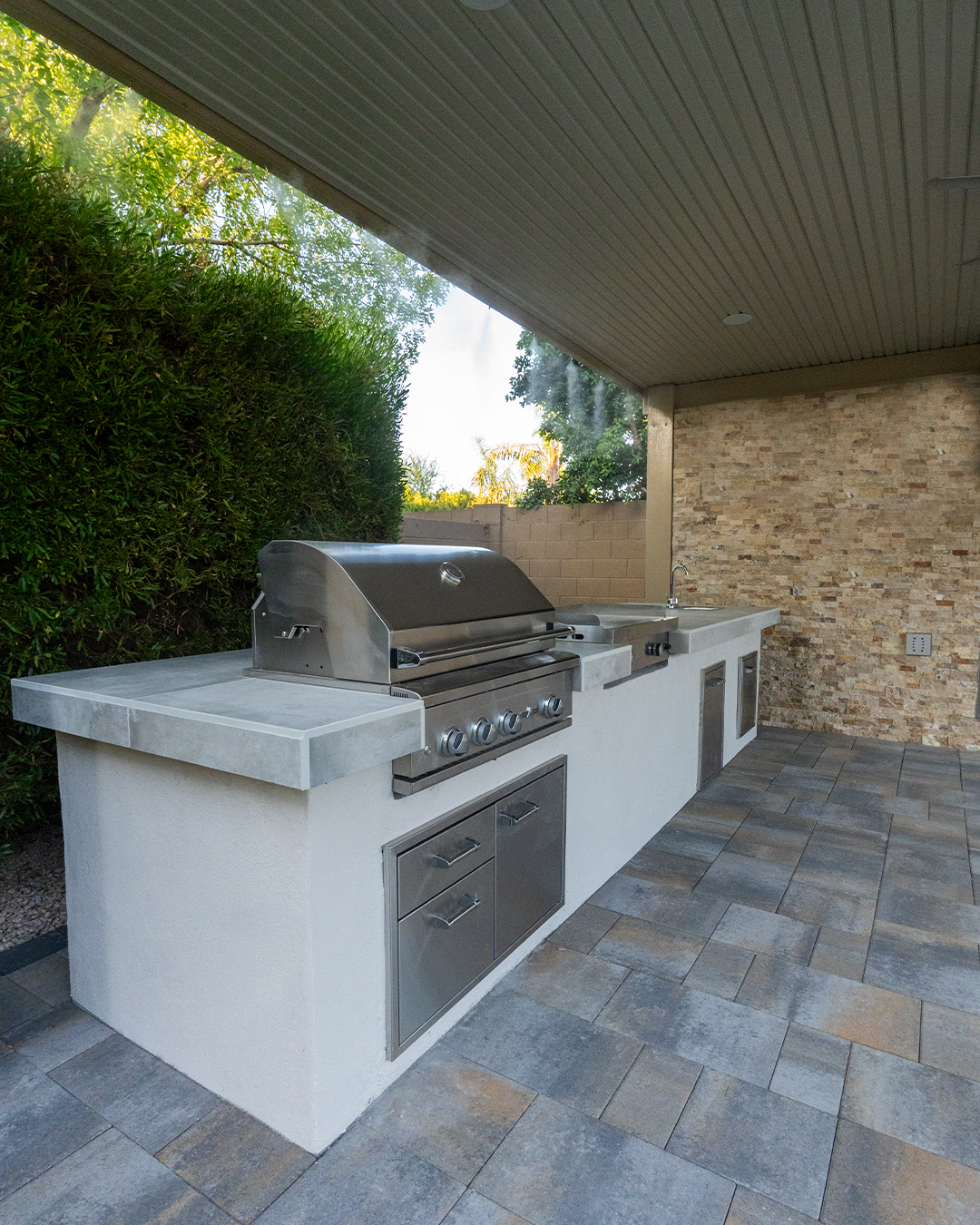 Outdoor kitchen island with stainless grill, sink and storage doors on a paver patio