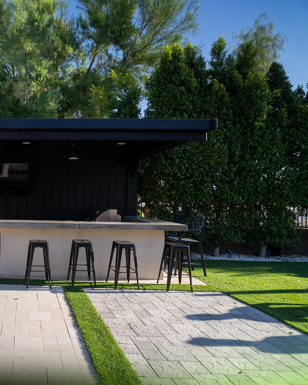 Outdoor kitchen bar with black stools on a paver patio