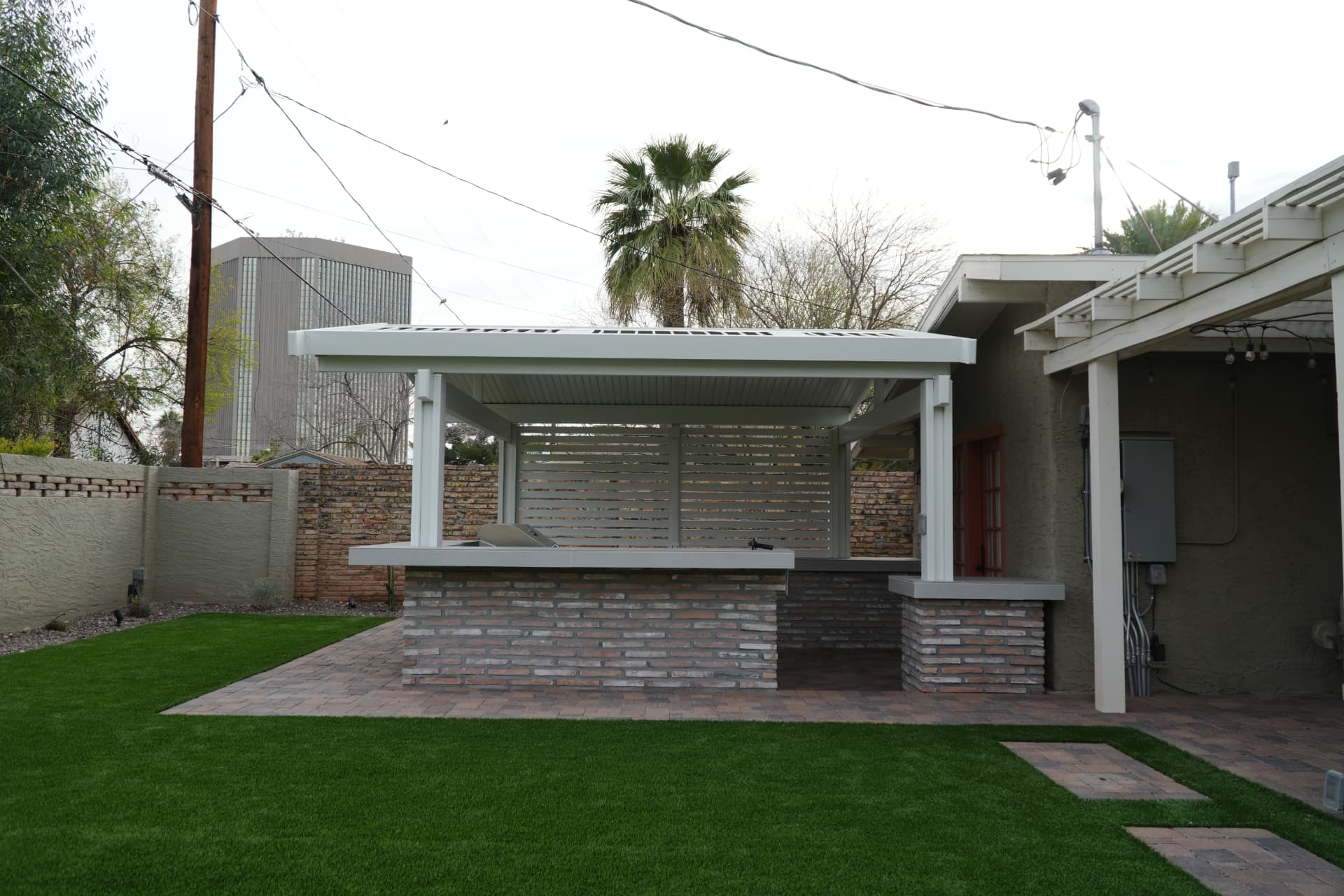 White louvered patio cover with slat privacy screen over a brick outdoor kitchen