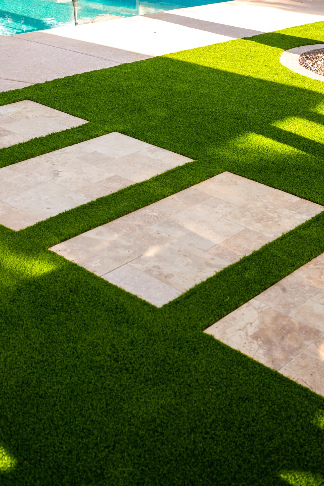 Travertine pavers inlaid in artificial turf near a pool