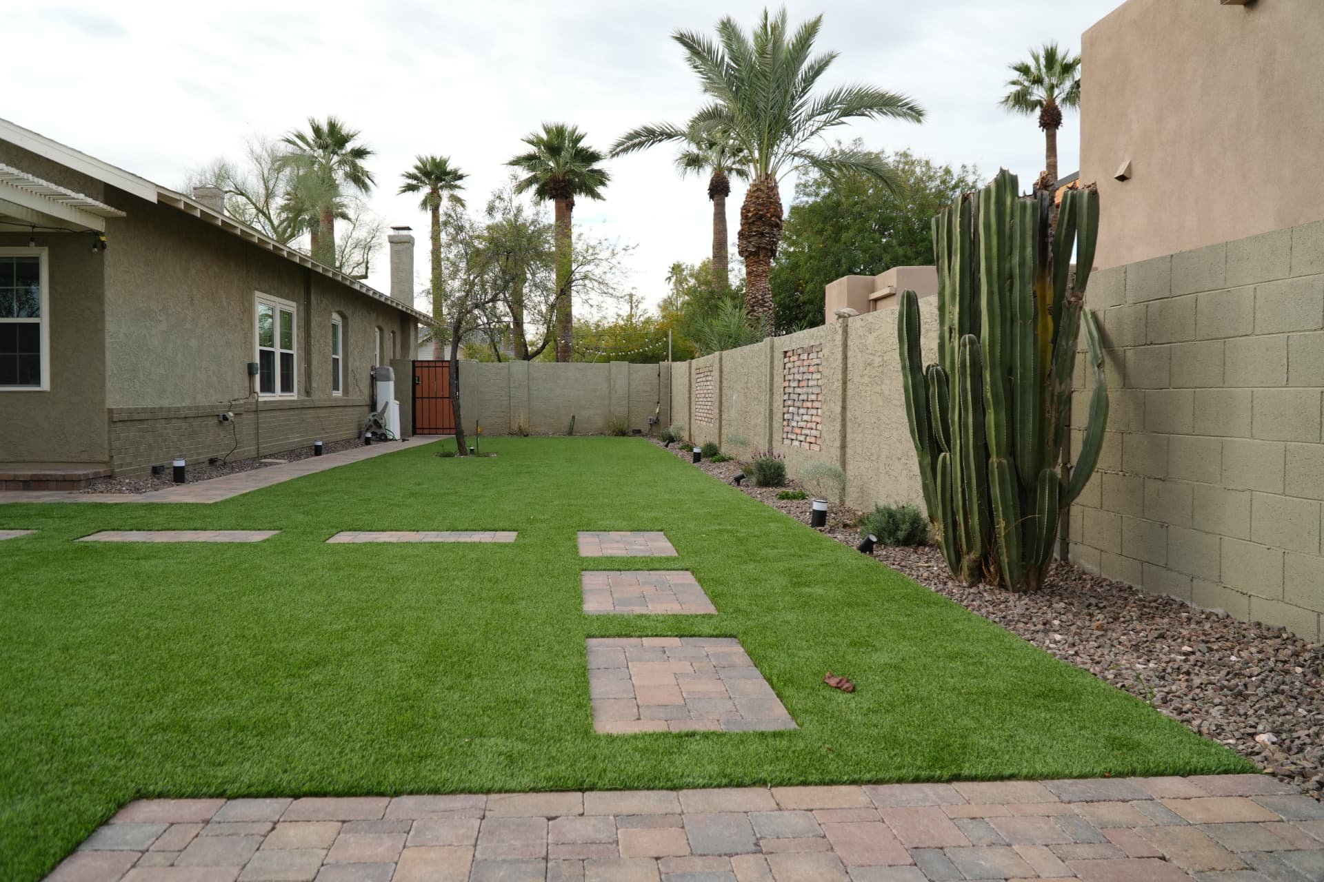 Artificial turf lawn with large paver stepping stones and a cactus against a block wall