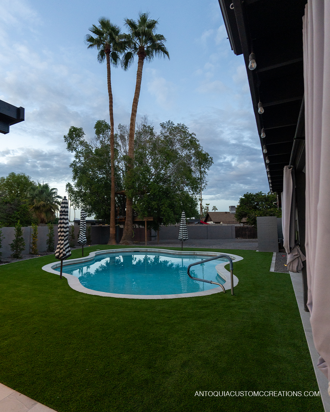 Freeform pool surrounded by artificial turf with palm trees at dusk