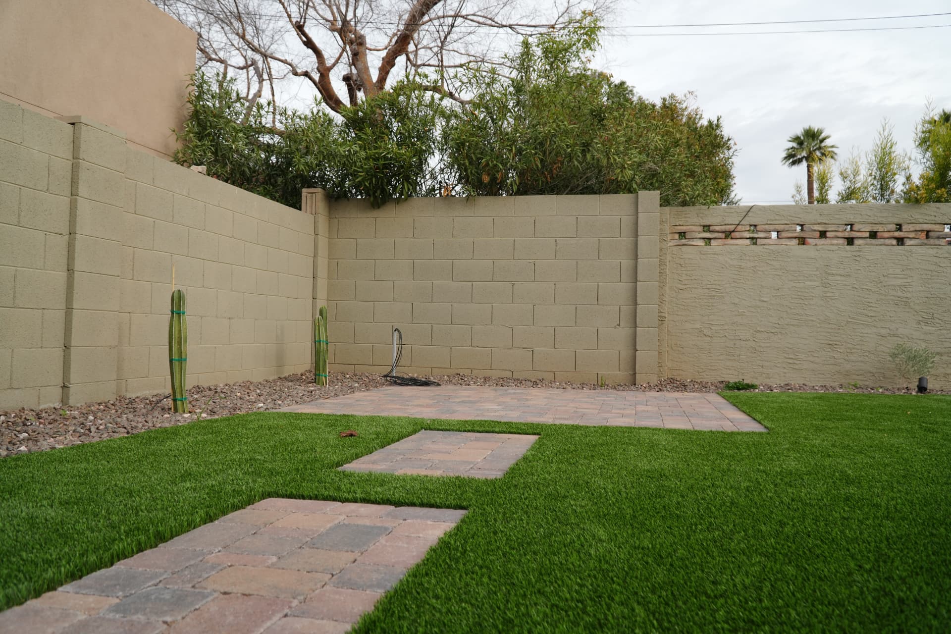 Corner paver patio pad meeting artificial turf with cacti along a block wall