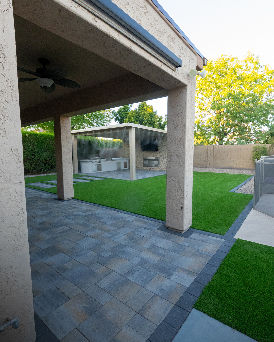 Covered rear patio with banded paver flooring opening onto turf lawn and pavilion